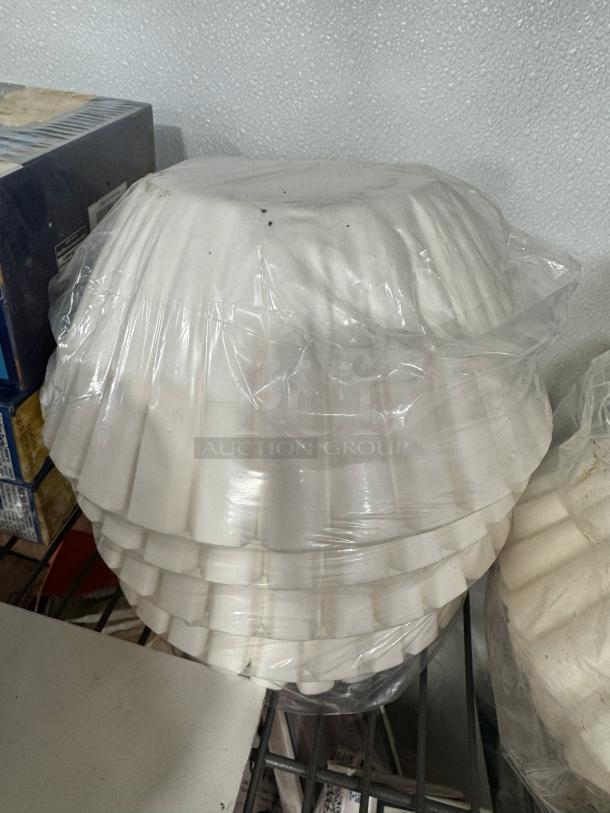 White coffee filters in unopened plastic packaging, stacked on a shelf. Suitable for drip coffee makers. Condition appears new.