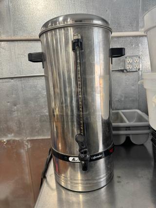 Stainless steel coffee urn/percolator with a black spout and handles, built-in level gauge, and "All American Coffeemaker" label.