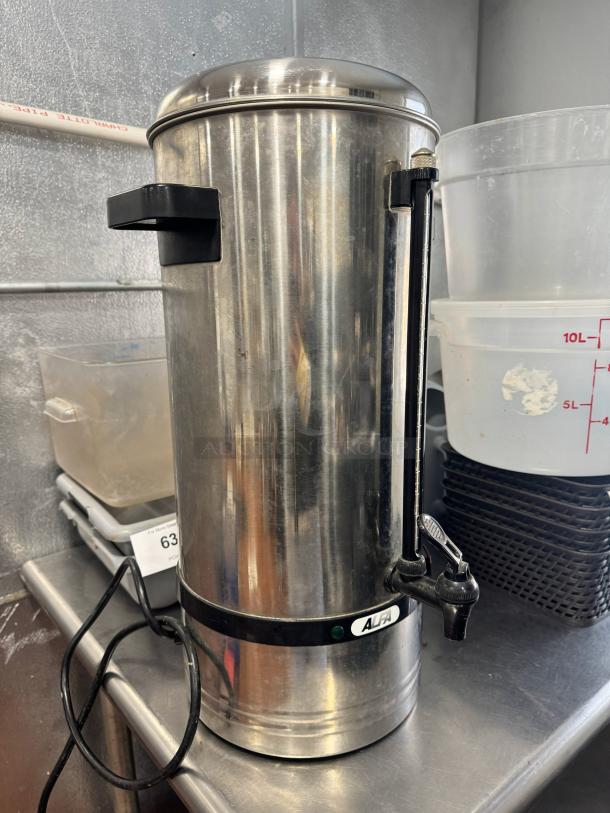 Stainless steel coffee urn, ALFA brand, commercial size, with spigot and power cord, minor surface wear, on metal counter.