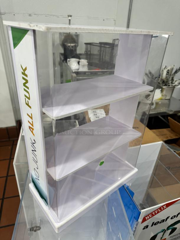 Acrylic display cabinet with three shelves, clear sides, and a "NO JUNK ALL FUNK" label; suitable for collectibles or retail.
