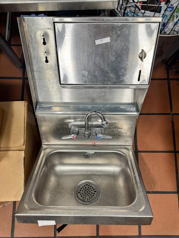 ADVANCE TABCO stainless steel wall-mounted hand sink with faucet, soap dispenser, and paper towel holder. Visible minor wear.