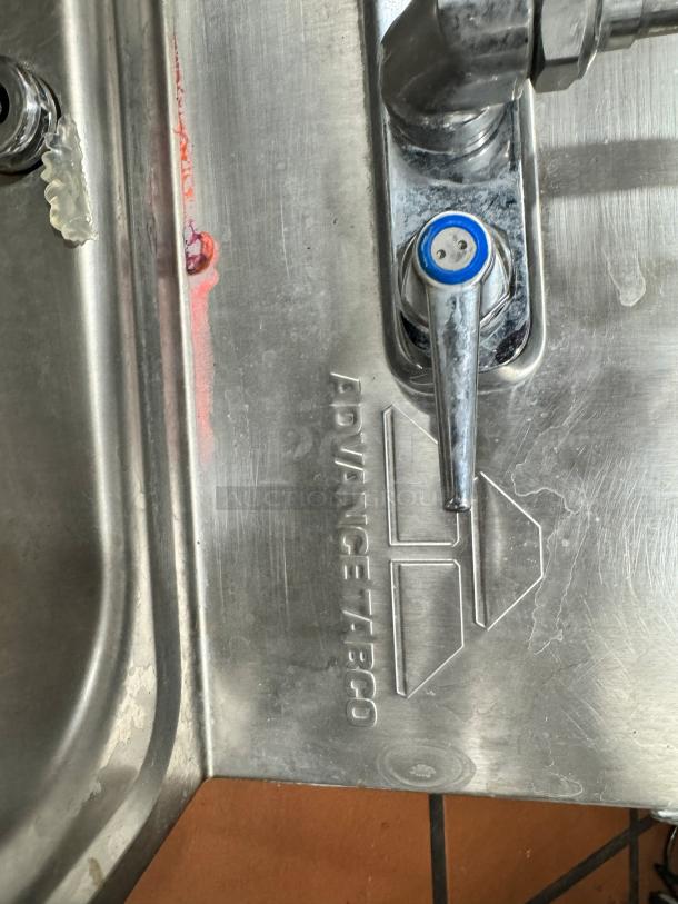 ADVANCE TABCO stainless steel hand sink with soap and paper towel dispenser, wall-mounted, embossed logo visible.