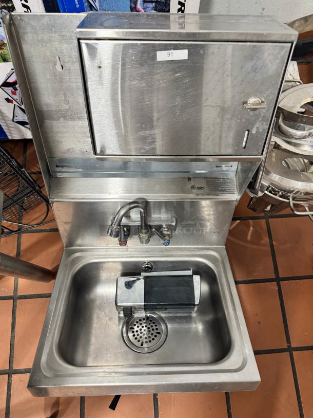 ADVANCE TABCO stainless steel wall-mounted hand sink with soap and paper towel dispenser. Features dual faucets, good condition.