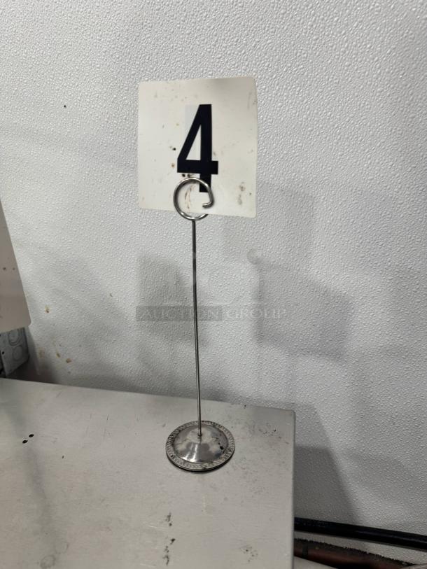 A metal table card holder with round base and a ring clip holding a numbered card "4." Part of a lot of 26, all sold together.