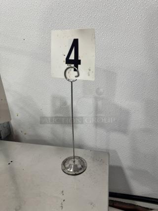 A metal table card holder with round base and a ring clip holding a numbered card "4." Part of a lot of 26, all sold together.