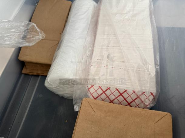 Lot of disposable food supplies, including white paper dishes, brown trays, and paper food trays with red pattern, in plastic wrap.