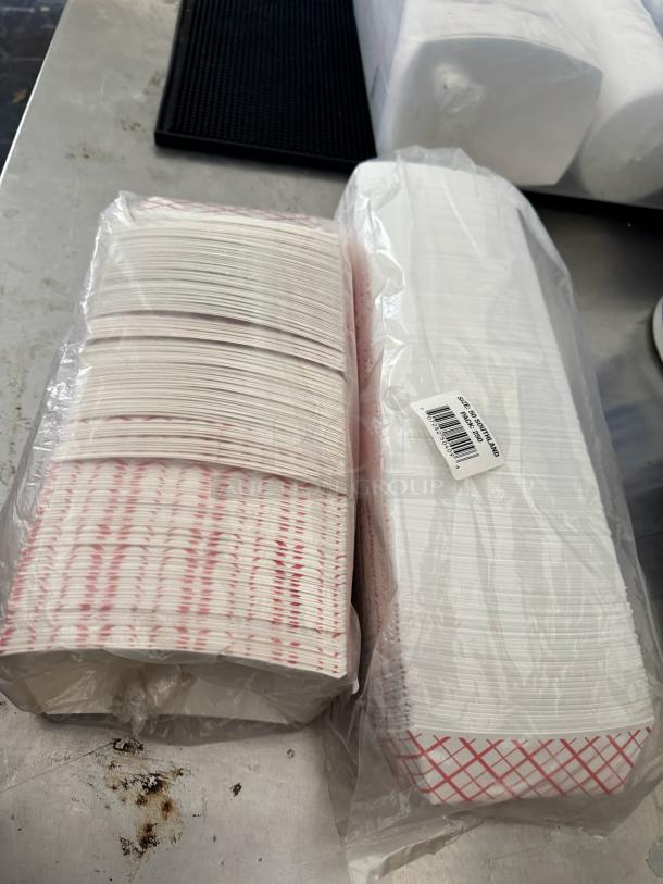 Stacks of disposable paper food trays, shrink-wrapped, red checkered pattern, in new condition.