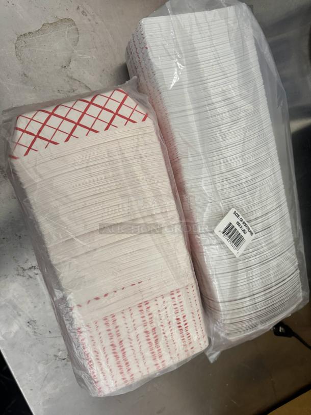 Stacks of disposable paper food trays in plastic packaging, featuring red grid and stripe designs. Label shows "Size 55" and a barcode.