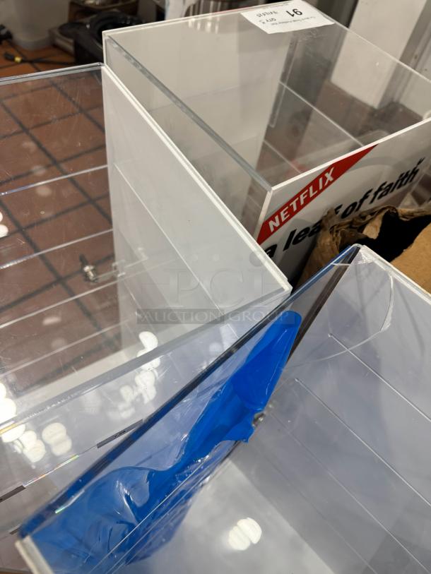 Acrylic Display Cabinet BIDX3, clear acrylic, sections for storage, visible Netflix branding, auction tag marked "97".