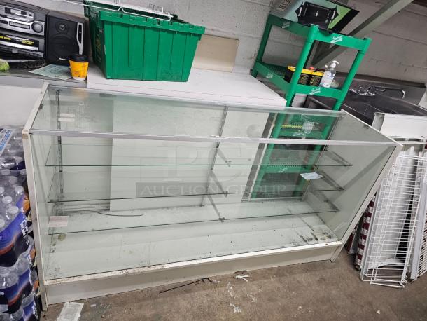 6ft glass display case BIDX2, with three shelves, metal frame, minor wear visible, suitable for retail or exhibition use.