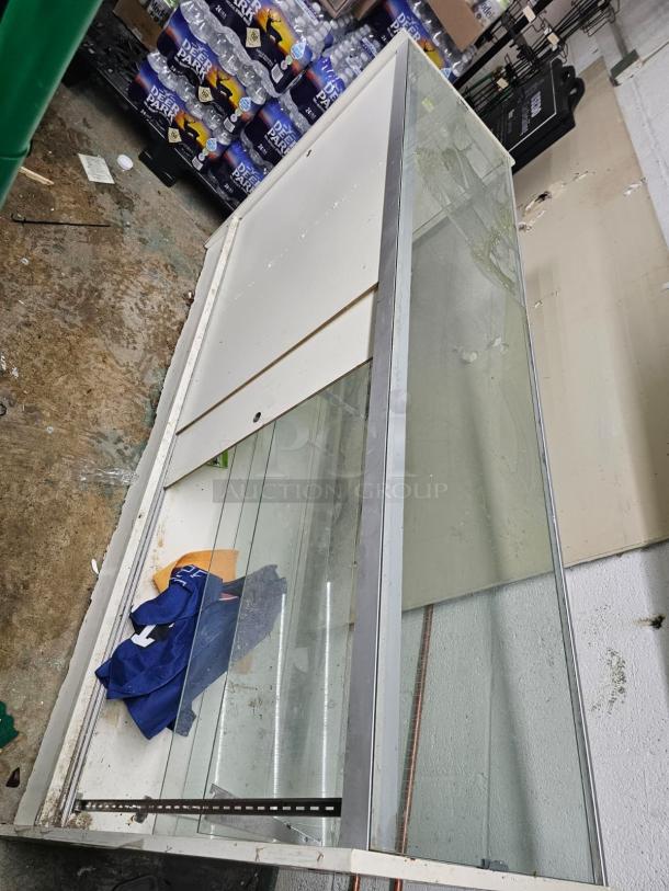 6ft glass display case BIDX2, metal frame, visible wear and dirt, sliding glass doors, suitable for retail use.