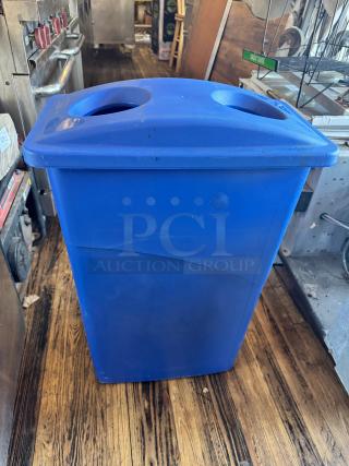 23-gallon blue slim recycling bin, dual circular openings on lid, in used condition, shown on wooden floor.