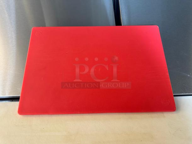 Red cutting board with visible surface scratches, made of durable plastic. Embossed NSF logo indicates food safety certification.