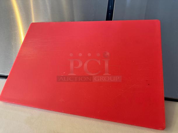 Red cutting board with minor scratches, rectangular shape, durable plastic, shown on a reflective surface.