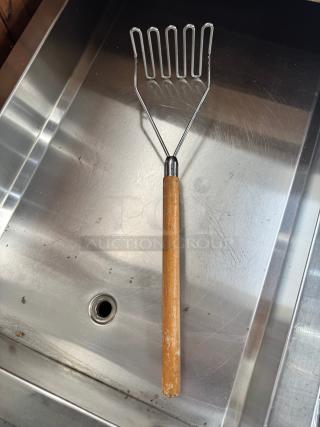 24" potato masher with wooden handle, metal mashing head. Shows wear, suitable for heavy-duty kitchen use.