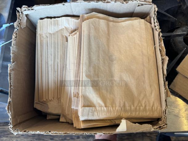 Cardboard box filled with multiple brown paper bags, slightly worn, labeled "ALL ONE MONEY."