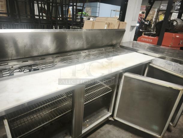 Heavy-duty 3 door refrigerated sandwich prep table, stainless steel, visible shelving, minor surface wear, ideal for commercial use.