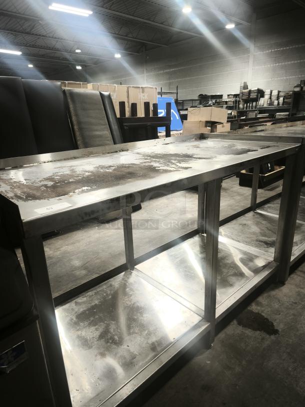 Stainless steel table with one shelf, showing signs of wear and rust. Ideal for warehouses or kitchens.
