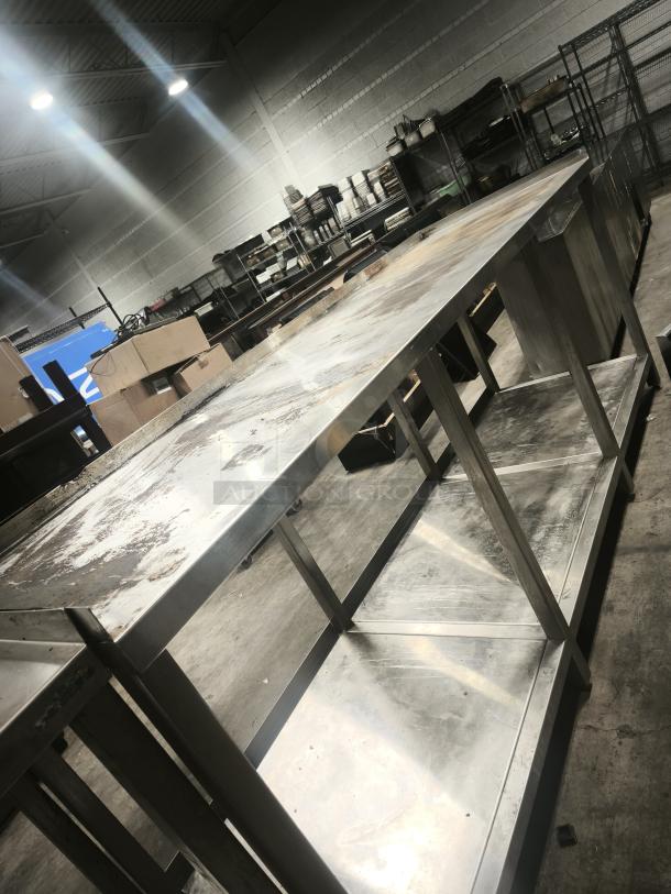 Stainless steel table with one shelf in an industrial setting, showing wear and surface stains.
