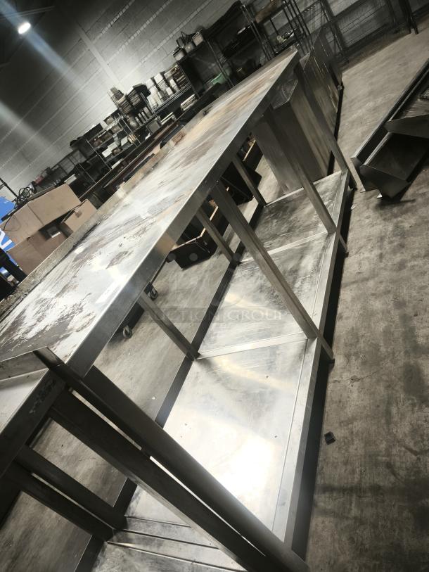 Stainless steel table with 1 shelf, showing signs of wear. Sturdy construction, ideal for industrial or kitchen use.