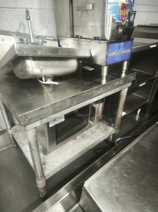 Stainless steel table with one shelf, slightly worn. Includes iced tea dispenser and small sink. Ideal for commercial use.