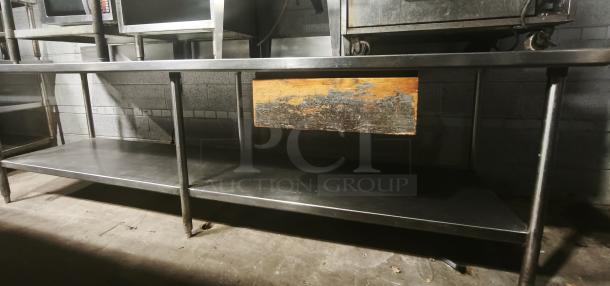 Stainless steel table with one shelf. Industrial style, slightly worn. Ideal for kitchen or workshop use. Sturdy design.