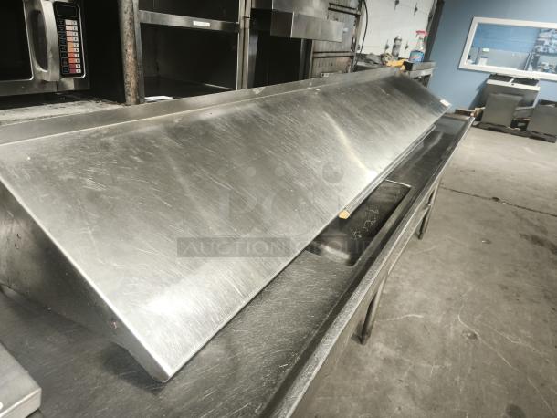 Stainless steel kitchen shelf with angled design, used condition, visible scuffs, sturdy construction, ideal for restaurant use.