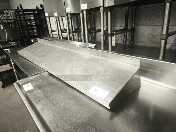 Stainless steel kitchen shelf, in good condition, features a sloped design. Numbered tags indicate potential auction details.