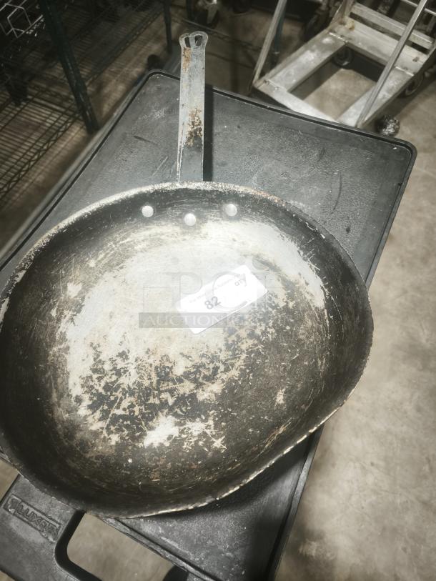 Stainless clad frying pan, 16-inch, heavily worn with visible scratches, attached riveted metal handle, auction tag number 82.