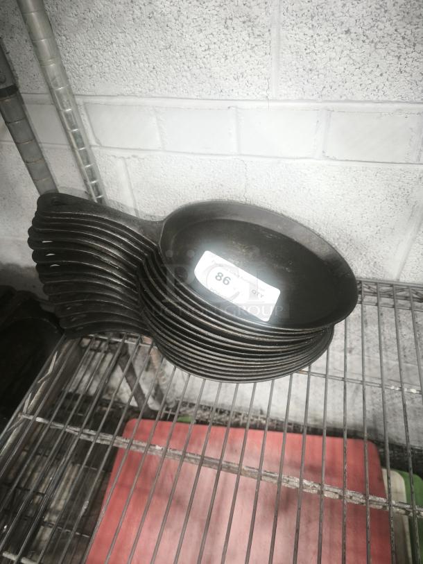 Lodge 10 x 7.5 inch cast iron oval serving griddle with teardrop handle; stack of several pans, black.