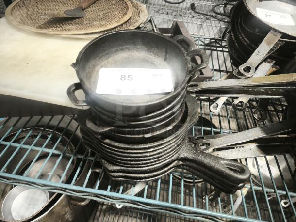 Pre-seasoned mini cast iron round casserole dish, stacked with others. Tag reads "85 QTY." Good condition, robust handles.