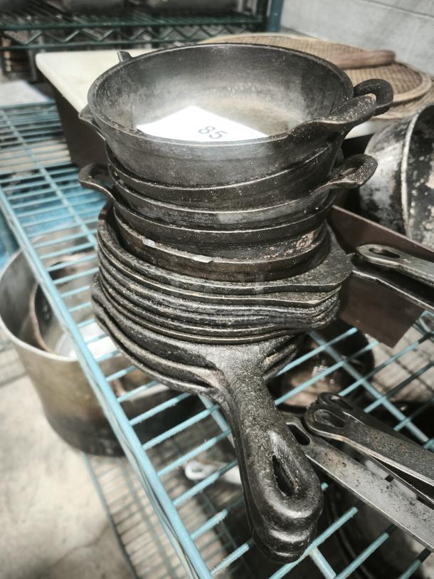 Pre-seasoned mini cast iron round casserole dishes stacked, showing signs of use. Tag marked "85."