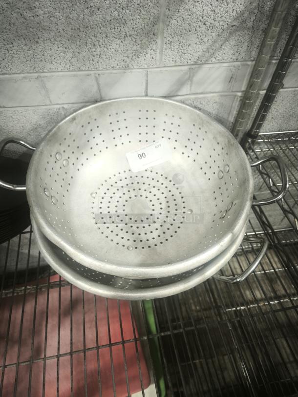 Heavy aluminum colander with handles and round base, showing slight wear. Quantity label visible.