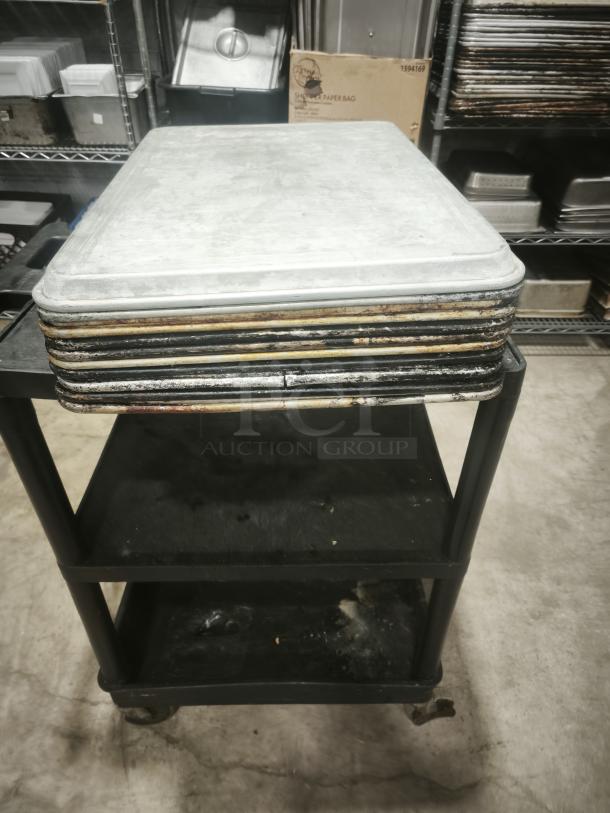 Multiple metal sheets stacked on a wheeled cart in an industrial kitchen setting.