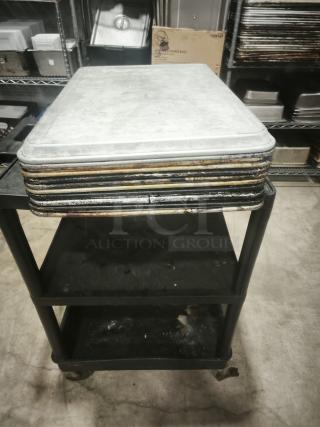 Multiple metal sheets stacked on a wheeled cart in an industrial kitchen setting.