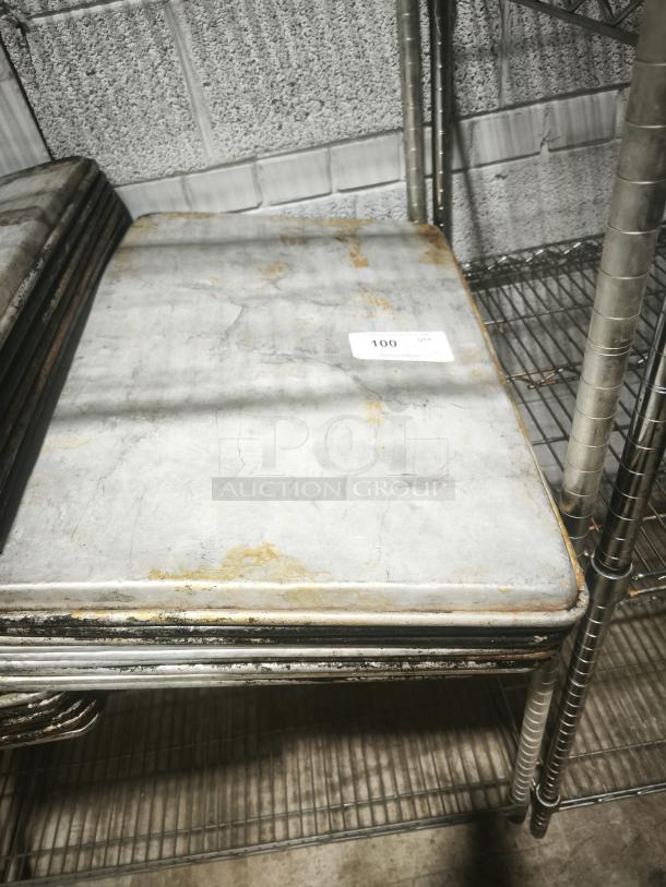 Square aluminum cake baking pan with visible wear and rust stains, stack of similar pans on metal shelving in industrial setting.