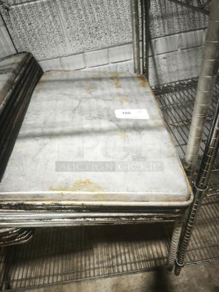 Square aluminum cake baking pan with visible wear and rust stains, stack of similar pans on metal shelving in industrial setting.