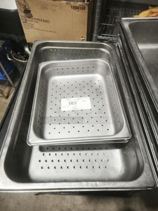 Full-size rectangular food pans, perforated, stainless steel, stacked on a shelf. Condition appears used. Auction label visible.