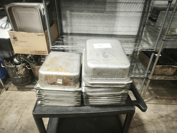 Stainless steel steam table pans, half full size, 4" deep, used condition with visible wear, stack of six with labels.