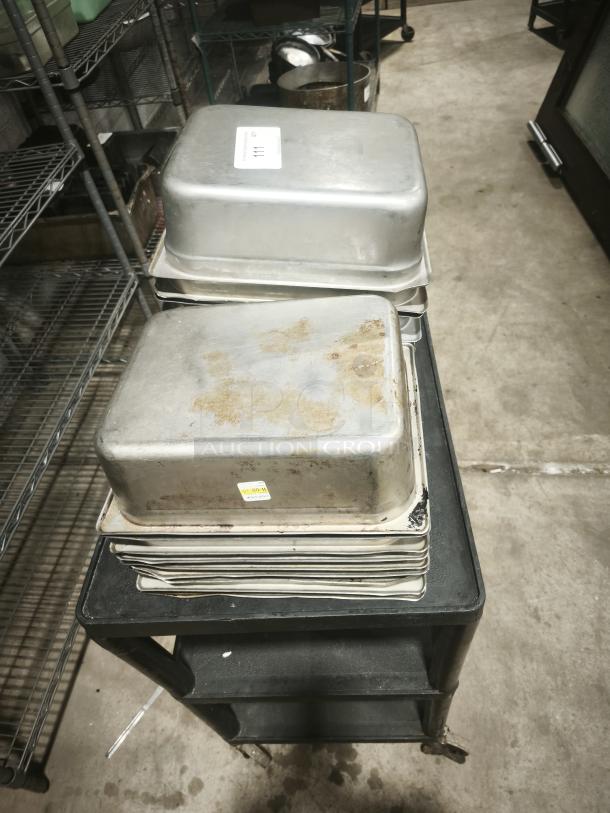 Stainless steel steam table pans, half full size, 4" deep, stacked on a cart, showing wear and patina from use.