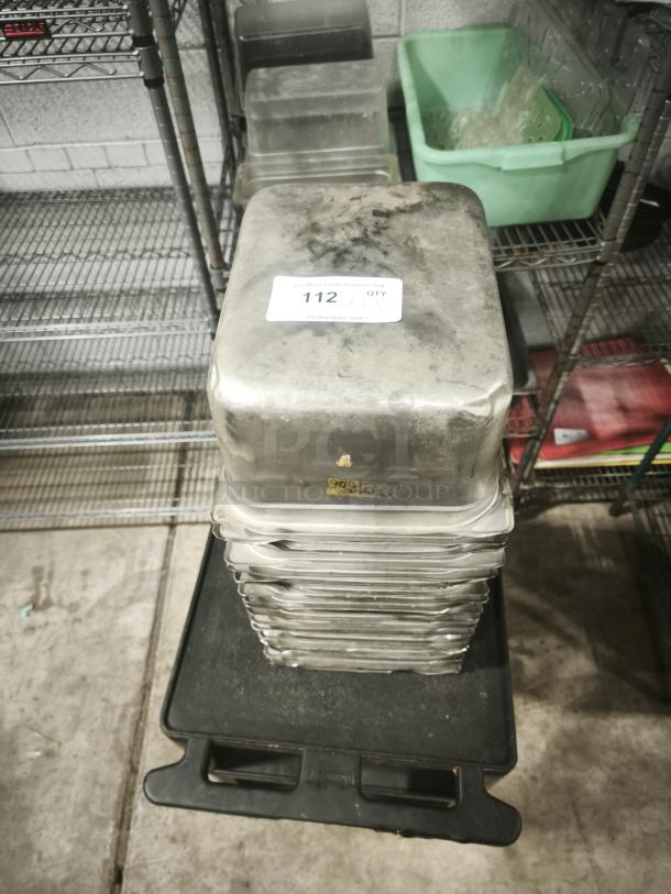 Stainless steel steam table pans, half full size, 6" deep, stacked, with visible wear. Auction label "112 x 19".