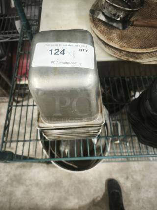Stack of 1/4 full-size pans, metal, minor wear, with auction lot label "124 x 8 QTY", stored on a wire shelf.