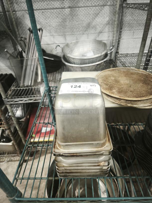 Stack of 1/4 full-size pans on a metal shelf, stainless steel, visibly used with wear marks. Label reads "124 x 8 QTY."