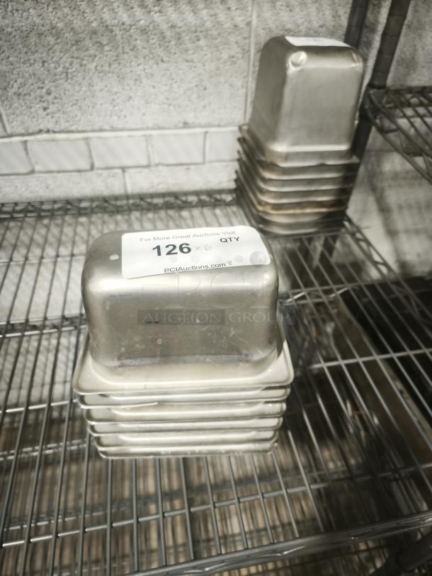 Stack of 1/9 size, 4" deep stainless steel food pans on a metal shelf, condition used. Label displays "126 x 6 QTY."