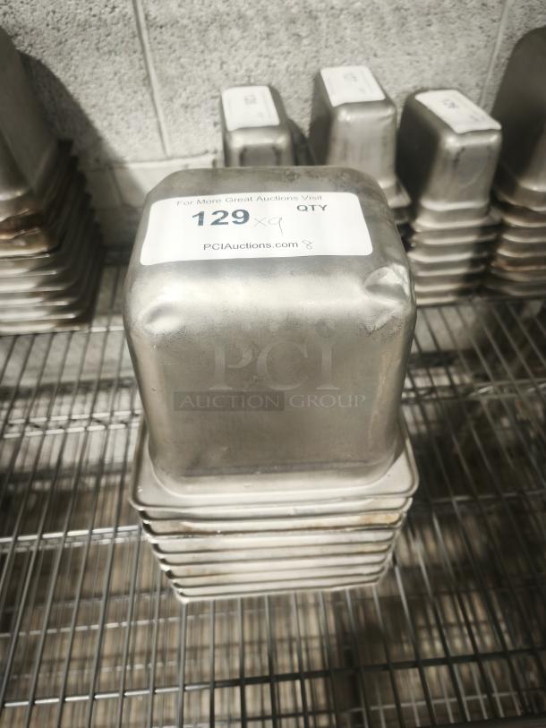Stack of 1/9 size, 4" deep stainless steel food pans, used, with auction label "129 x 9 QTY" on top pan.