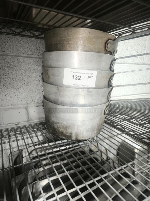 Stack of heavy gauge sauce pans on a wire shelf, in used condition. Marking tag reads "132 x 5 QTY."