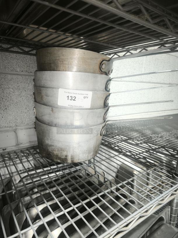 Heavy gauge sauce pans with long handles stacked on wire shelf, stainless steel, used condition. Label indicates lot 132.