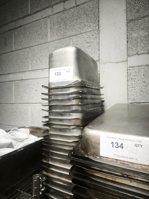 Stack of 1/3 size 4" deep metal food pans with visible auction labels, marked for quantity and auction site details.