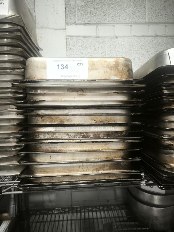 Stack of full size 4" deep food pans, used condition, with visible wear. Auction lot number 134 label on top pan.