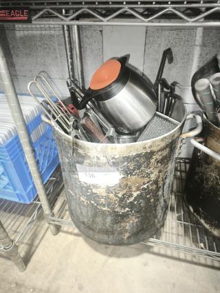 Large worn metal pan with assorted kitchen utensils inside, including a stainless steel pitcher with an orange lid. Numbered tag reads "136."
